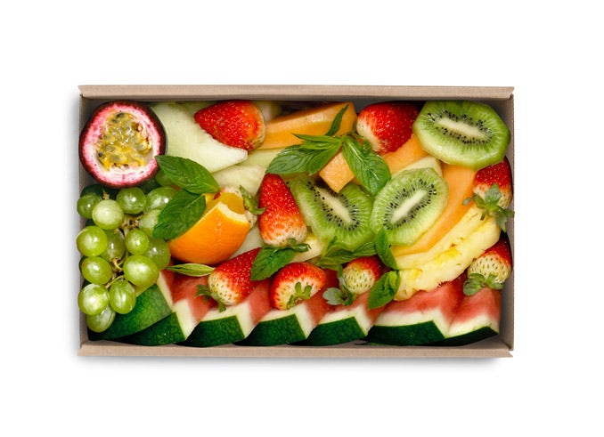 A box filled with assorted fresh fruits—watermelon, strawberries, green grapes, kiwi, passion fruit, pineapple, melon slices, and mint leaves—neatly arranged on an Extra Small BioBoard Catering Tray.