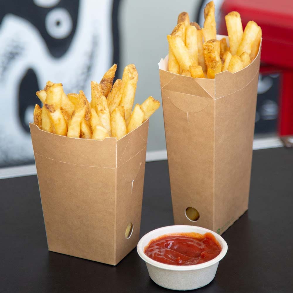 Two Chip BioBoard Boxes filled with French fries sit on a black surface, with a small cup of ketchup in front of them.